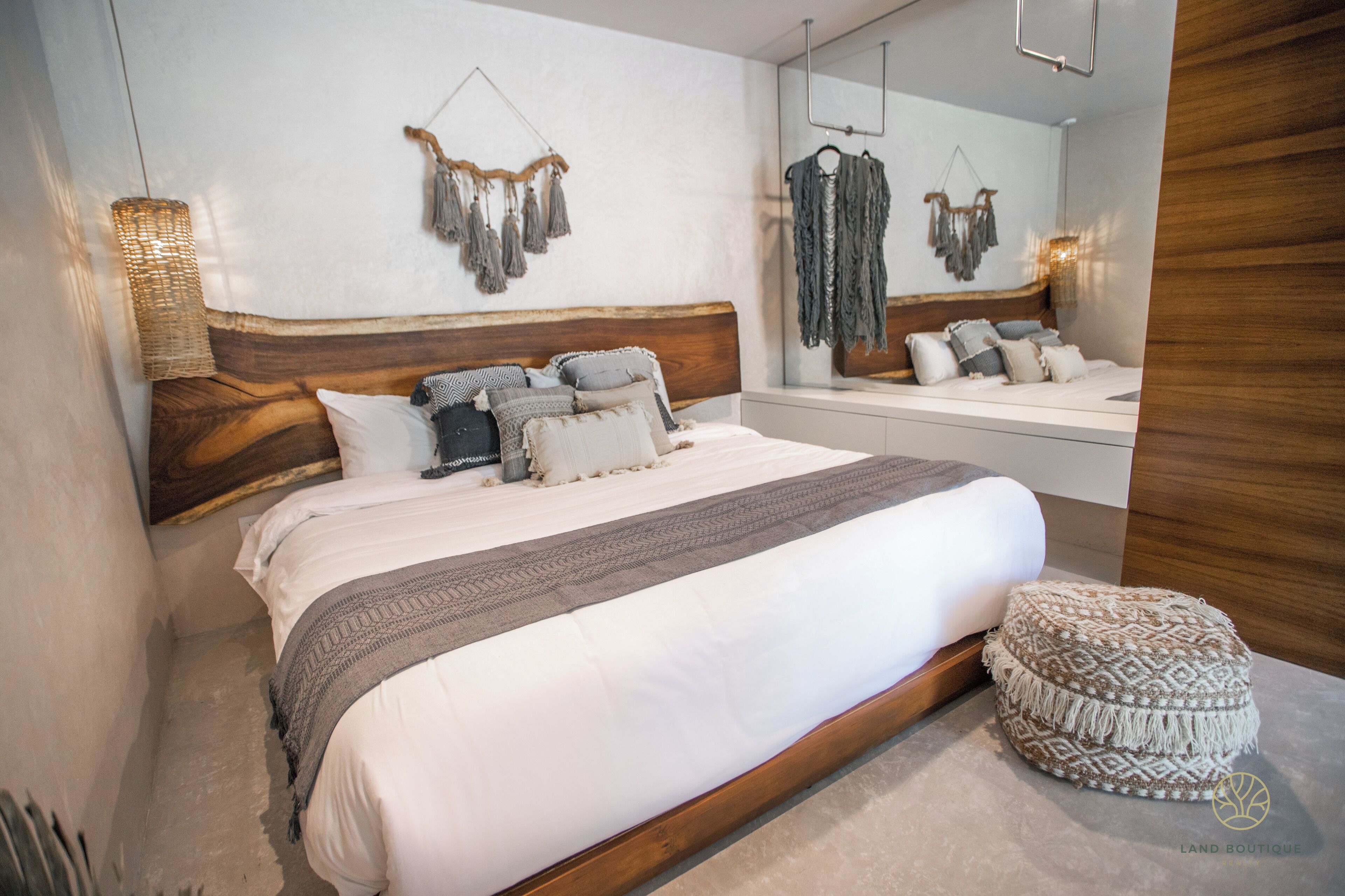 Een slaapkamer met een groot bed, een houten hoofdbord, een nachtkastje, een spiegel en een macramé decoratie.