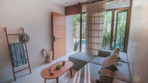 A modern living room with a sofa, a wooden table, and a view of greenery through a sliding door. - Jungle studio (Tulum)