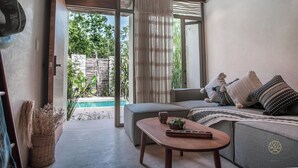 A modern living room with a sofa, a coffee table, and a view of a pool. - Jungle studio (Tulum)