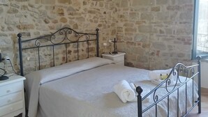Ein Schlafzimmer mit Steinwand, Metallbettgestell, Nachttisch in Weiß und einem Fenster mit Blick.