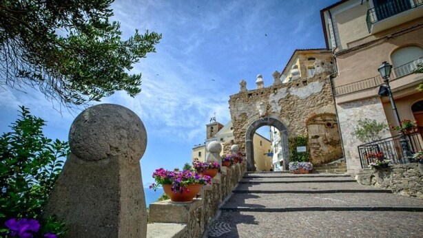 Eine Steintreppe führt zu einem historischen Gebäude mit Arkaden, umgeben von Blumentöpfen und traditioneller Architektur.