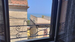 Ein Fenster mit Blick auf eine Küstenlandschaft, mit Gebäuden mit Ziegeldächern und blauem Himmel.