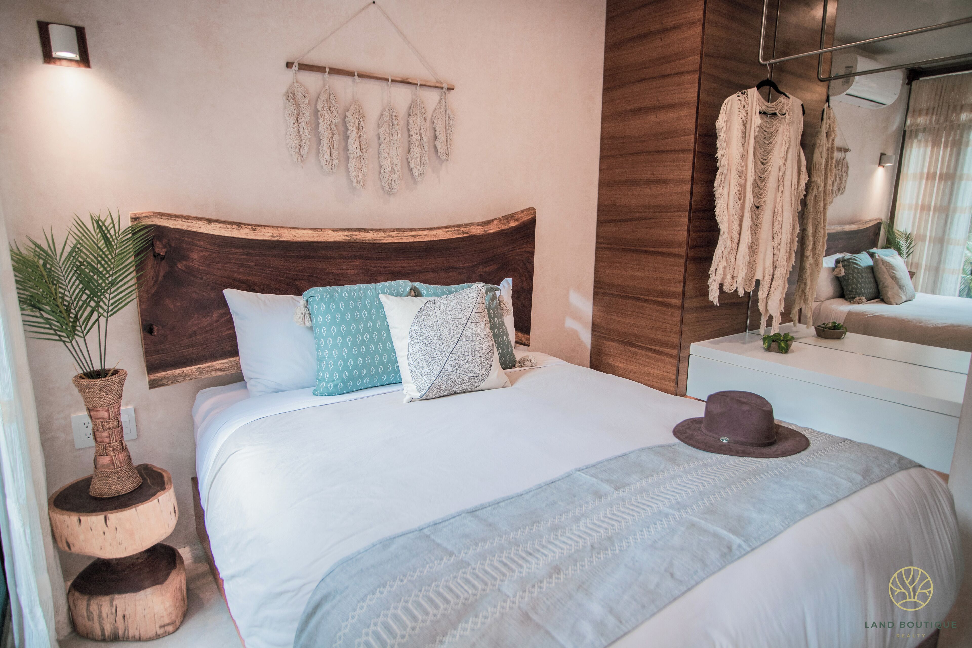 Un dormitorio ordenado con cabecera de madera, una planta en la mesita de noche y una percha para ropa.