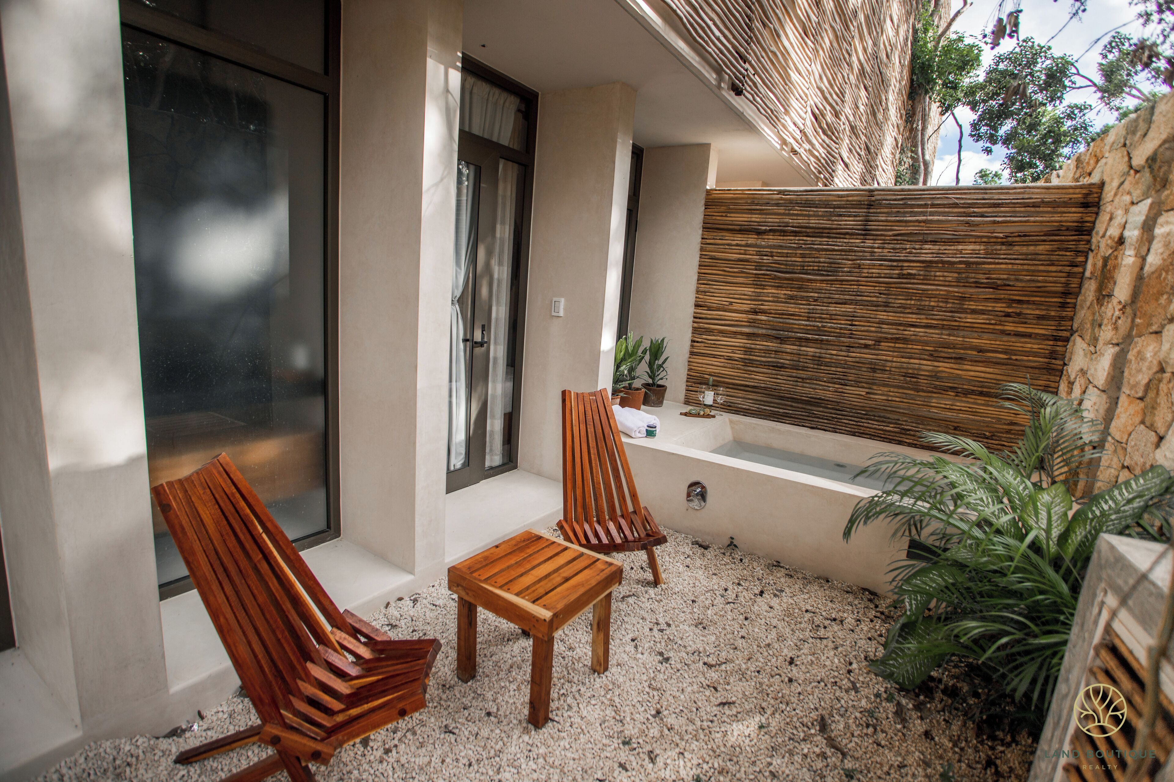 A patio area with two wooden chairs, a small table, a bathtub, and a potted plant.
