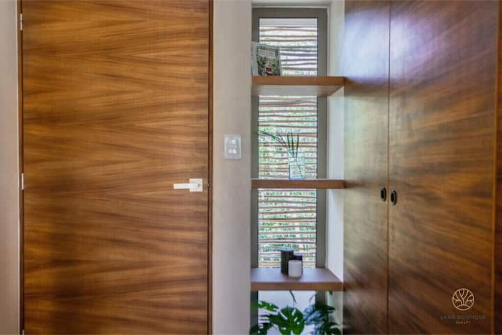 Ein Holzkleiderschrank mit Schiebetür, ein Fenster mit Jalousien und ein Regal mit einer Pflanze.