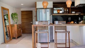 A modern kitchen with a central island, wooden chairs, and hanging pendant lights. - Stylish Jungle Studio · Outdoor Tub & Yoga Deck (Tulum)