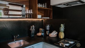 A modern kitchen with a built-in microwave, coffee maker, and a small stove. There is a sink with a faucet, a knife block, and a pineapple on the counter. - Stylish Jungle Studio · Outdoor Tub & Yoga Deck (Tulum)