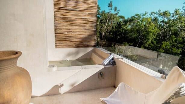 A balcony with a glass enclosure, a beige cushioned chair, and a terracotta pot. - Stylish Jungle Studio · Outdoor Tub & Yoga Deck (Tulum)
