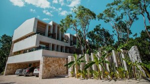 A modern multi-story building with a flat roof, large windows, and a parking area with cars. - Stylish Jungle Studio · Outdoor Tub & Yoga Deck (Tulum)
