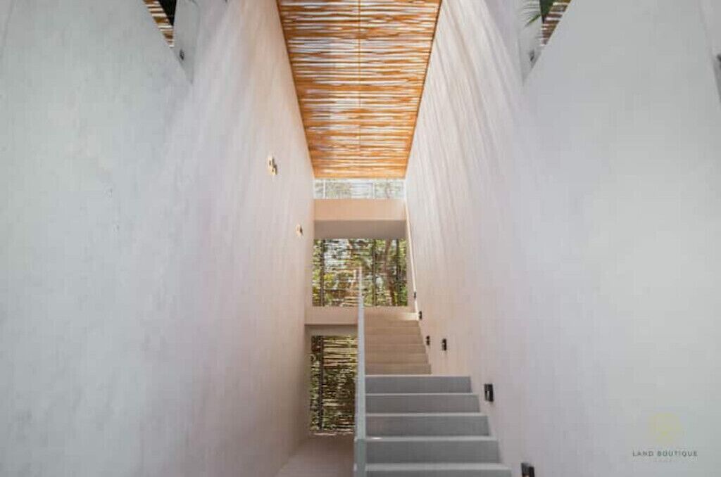 A modern interior with a staircase leading to a higher floor, white walls, and a wooden slatted ceiling.