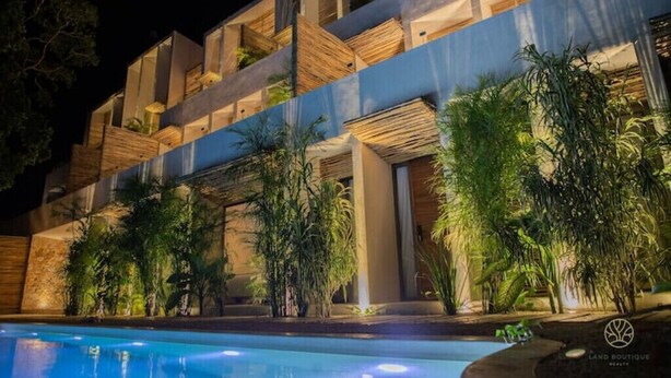 Un bâtiment moderne doté d’une piscine, avec des balcons ornés de plantes et une façade bien éclairée.
