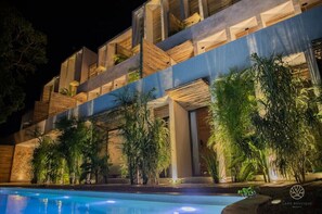 Un edificio moderno con piscina, caratterizzato da balconi con piante e una facciata ben illuminata.