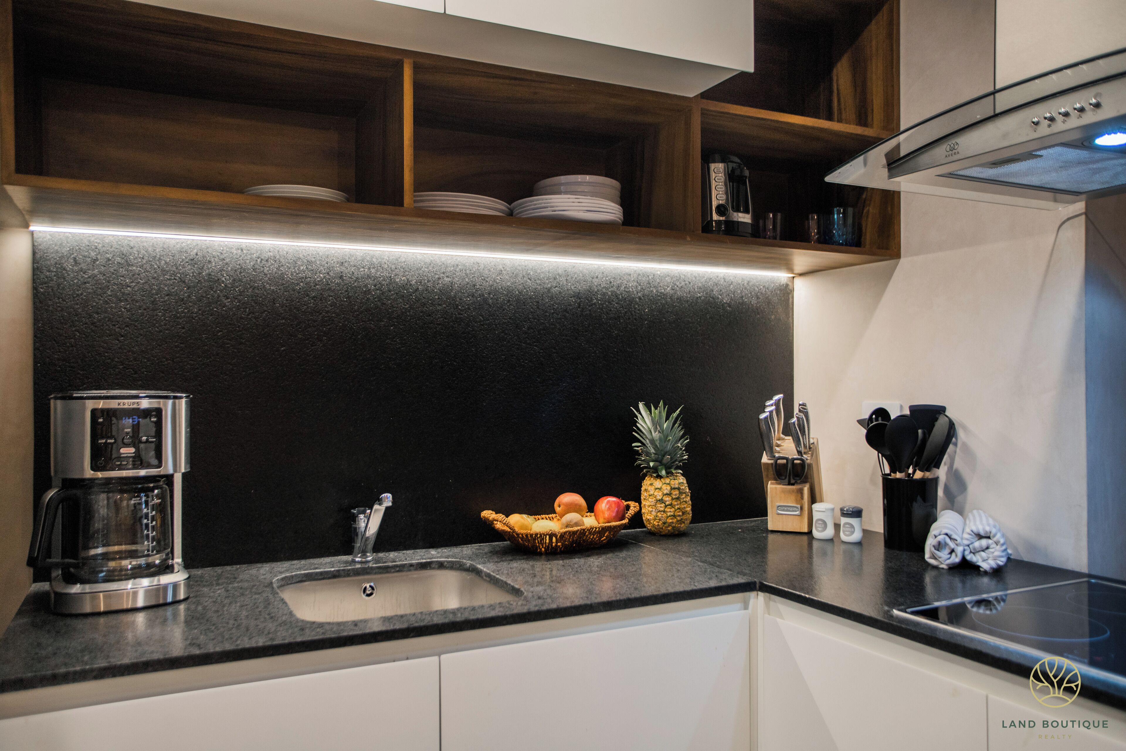 A modern kitchen with a black countertop, stainless steel appliances, and a fruit bowl.