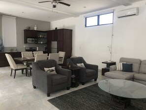 A modern living room with a dining area, dark wood cabinets, a kitchen in the background, and a ceiling fan.