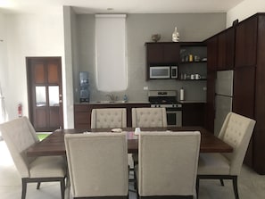 A modern kitchen with a dining table and chairs, a water dispenser, a microwave, a stove, and a refrigerator.