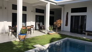 Un patio moderno al aire libre con piscina, rodeado de paredes blancas y grandes ventanales.