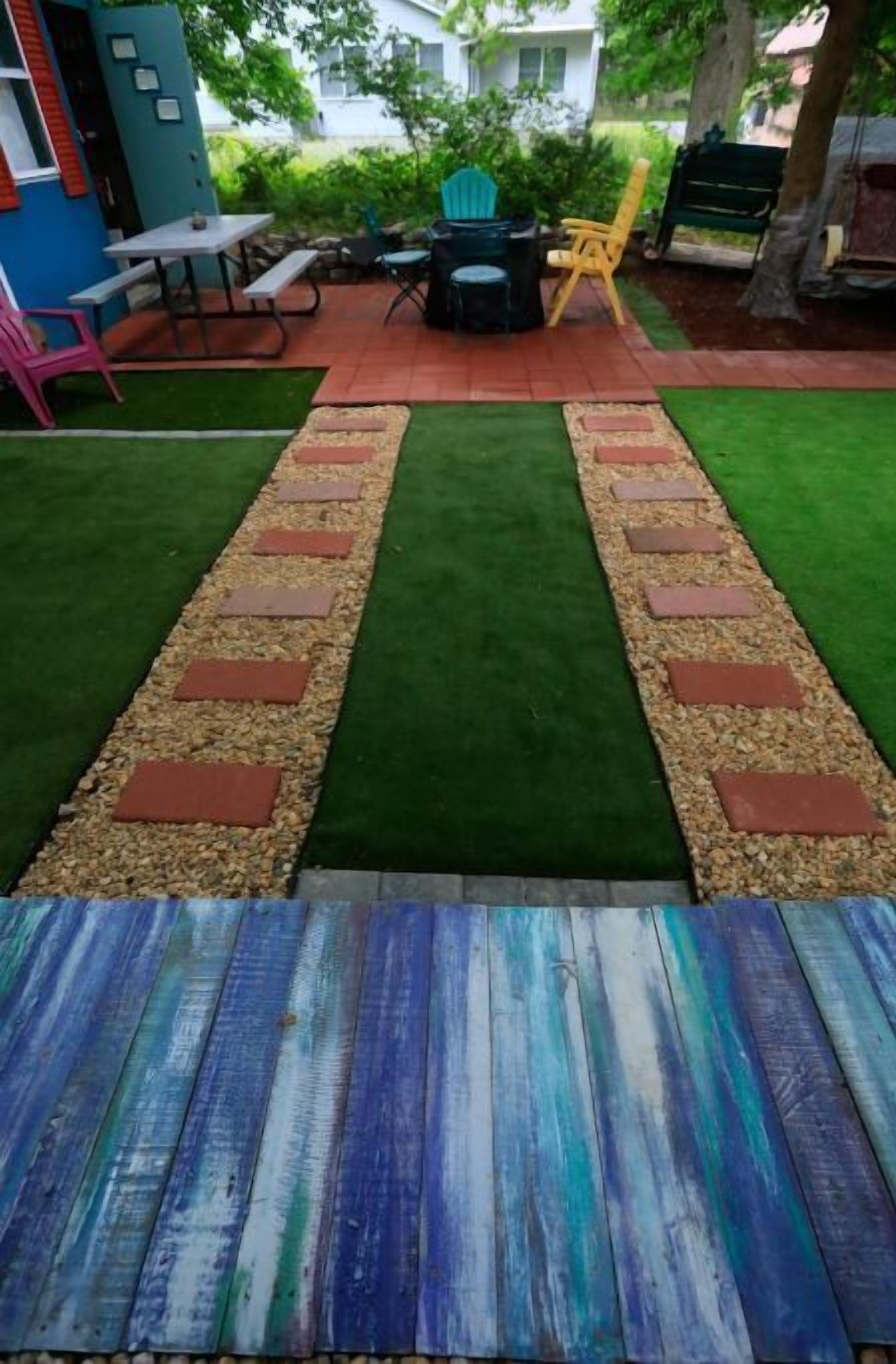 Un patio con mesa de madera, césped verde y una zona de estar con sillas y mesa.