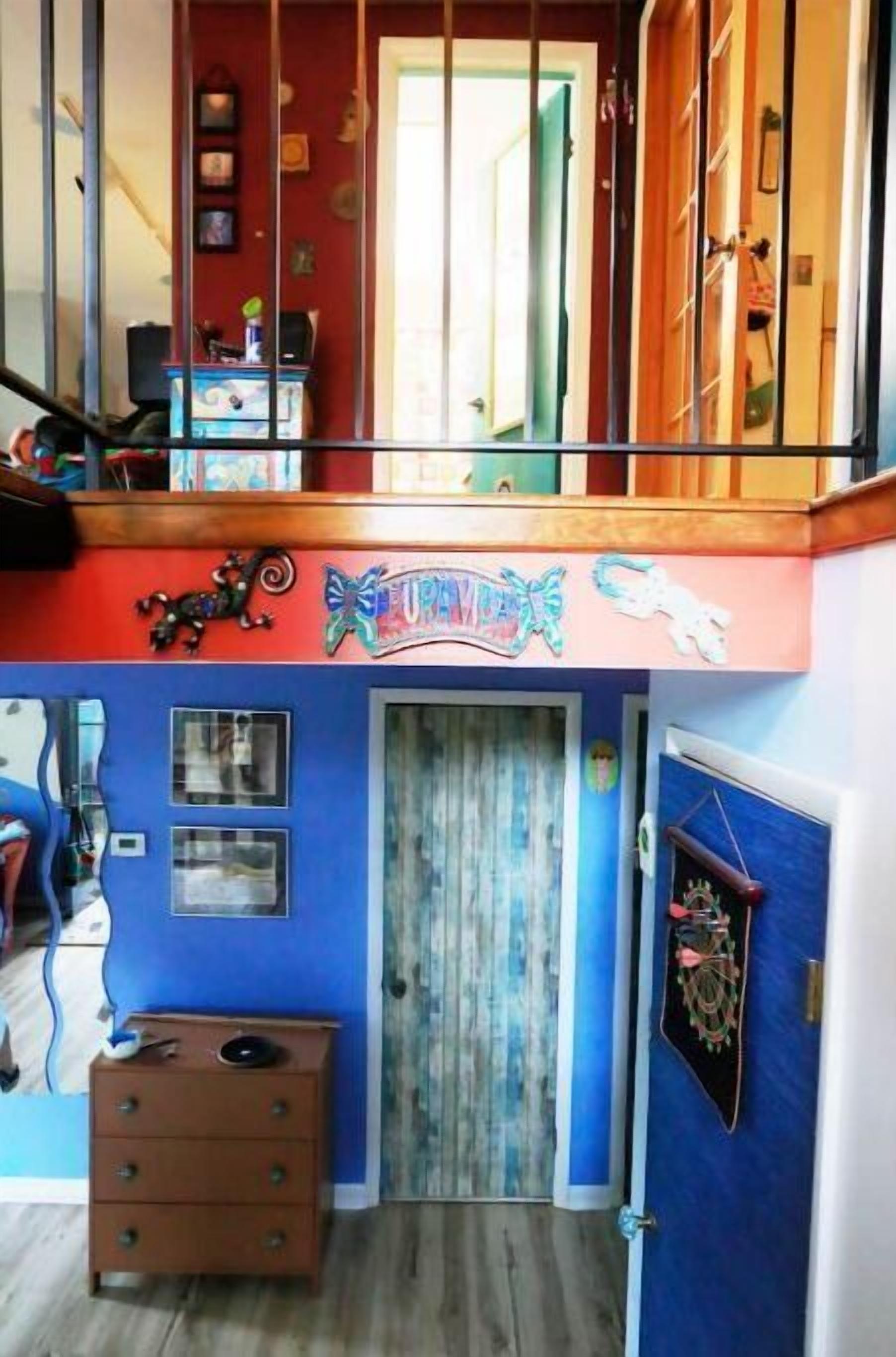Une pièce avec un mur bleu, une commode en bois, une porte avec un rideau et un escalier muni d’une rampe.