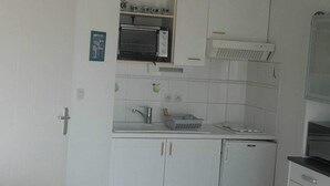 A compact kitchen with white cabinets, a built-in oven, a microwave, and a gas stove. - Appartement vue sur mer (Châtelaillon-Plage)