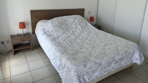 A neatly made bed with a floral-patterned duvet, two bedside tables with lamps, and a tiled floor. - Appartement vue sur mer (Châtelaillon-Plage)
