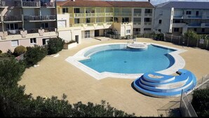 A pool area with a circular pool and a blue water slide, surrounded by multi-story buildings with balconies. - Appartement vue sur mer (Châtelaillon-Plage)