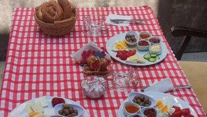 A table set with a red and white checkered tablecloth, two plates of food, a basket of bread, and a pink container. - Lavinya Pansiyon (Kusadasi)