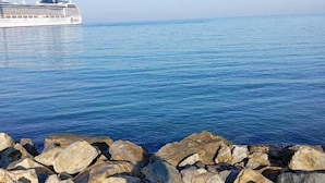 A cruise ship docked at a rocky pier with clear blue water and a calm sea in the background. - Lavinya Pansiyon (Kusadasi)