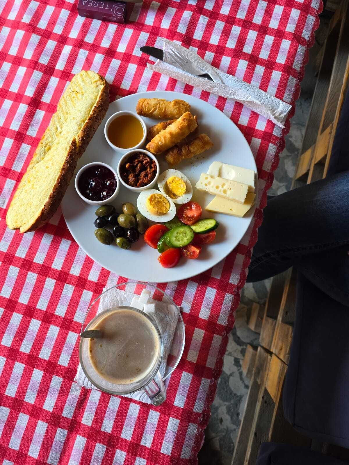 A meal with bread, eggs, cheese, vegetables, and a drink on a red and white checkered tablecloth.