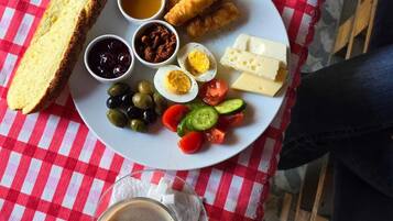 A meal with bread, eggs, cheese, vegetables, and a drink on a red and white checkered tablecloth.
