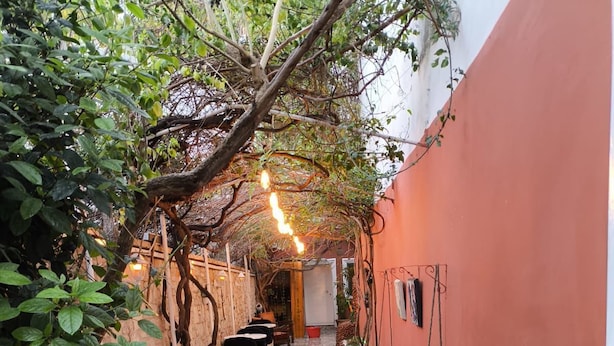 A narrow outdoor corridor with tiled flooring, tables, chairs, and a hanging light fixture. - Lavinya Pansiyon (Kusadasi)