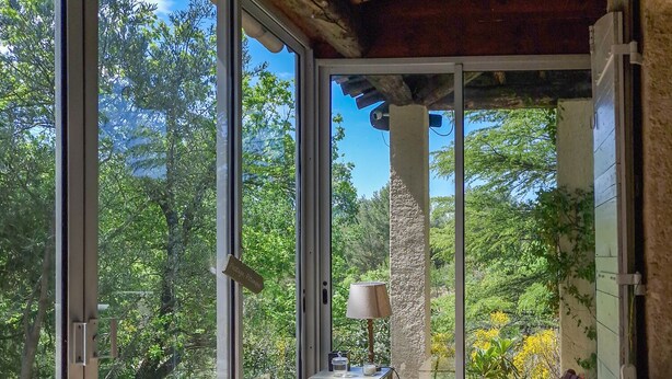A sunlit room with large glass doors, a small round table with a vase of flowers, and two wicker lounge chairs. - 3 bed + villa near Gordes with air-con, pool and stunning views over the Luberon (Cabrières-d'Avignon)
