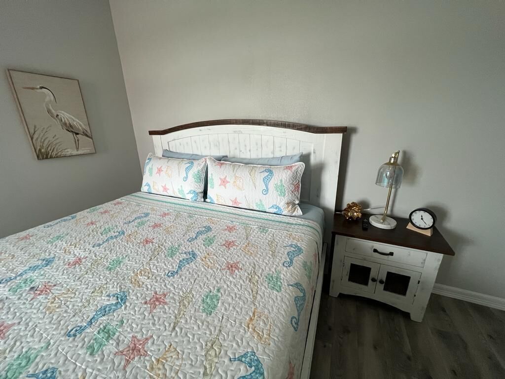 A bedroom with a bed, a nightstand, a lamp, and a clock.