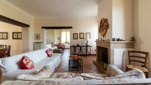 Een gezellige woonkamer met een bank, fauteuils, een open haard en een eethoek met een tafel en stoelen.