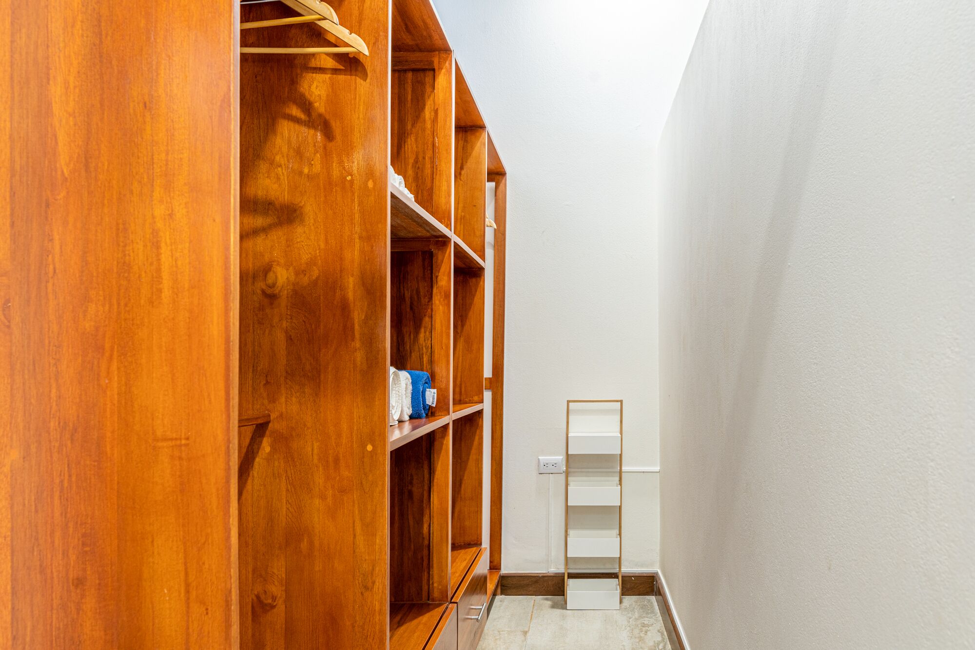 A narrow hallway with wooden shelving units on one side and a white wall on the other.