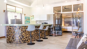 Une cuisine moderne dotée d’un îlot central, de tabourets de bar et d’un espace nuit séparé par une paroi de verre.