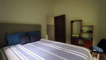 A bedroom with a bed, pillows, a chair, and a wooden shelf with folded clothes.