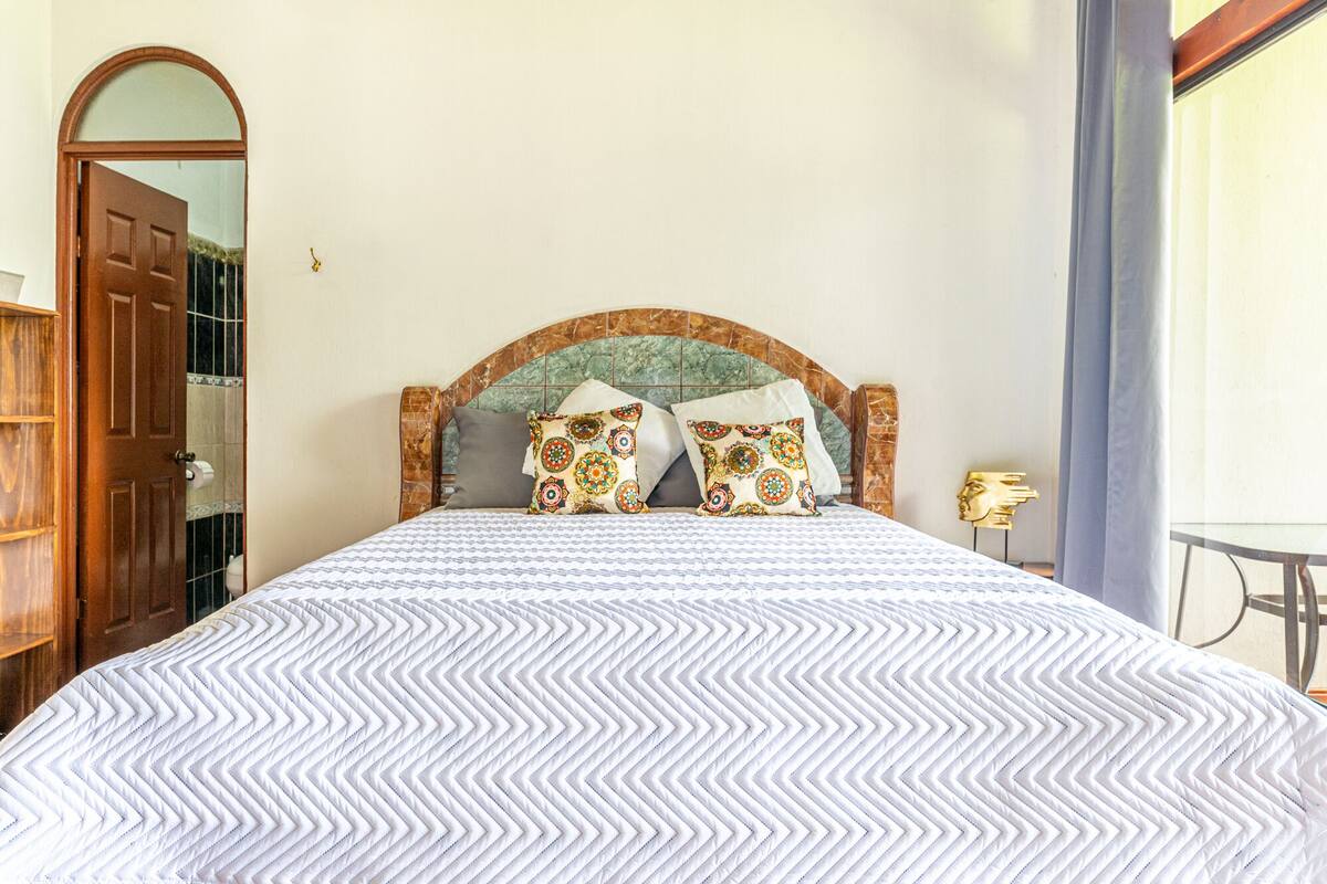 Una cama con una colcha estampada, un cabecero con un diseño decorativo y dos almohadas con un motivo geométrico.