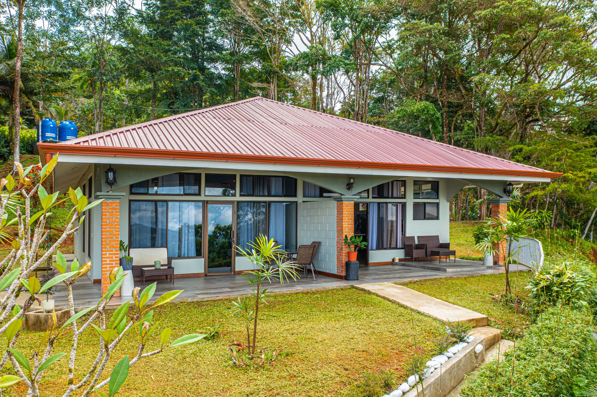 A modern house with a red roof, large windows, and a covered porch with outdoor furniture.