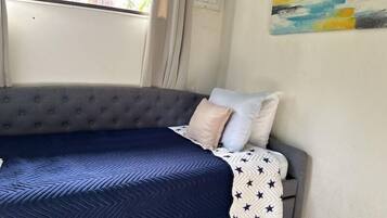 Un lit avec une couette bleue et une couverture à motifs, une tête de lit rembourrée grise et deux oreillers.