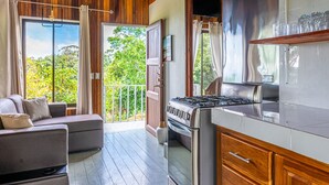 Une cuisine moderne équipée d’une cuisinière à gaz, de meubles en bois et d’un balcon offrant une vue sur la verdure.