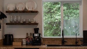 A kitchen with a window, a coffee machine, and various glassware on shelves.