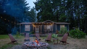 A cabin with a fire pit surrounded by chairs, a covered porch, and a deck.