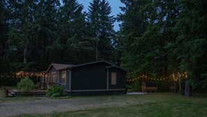 A cabin with a porch and string lights, surrounded by a forest.