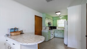 Une cuisine avec des meubles blancs et verts, un plan de travail en marbre et une porte en bois.