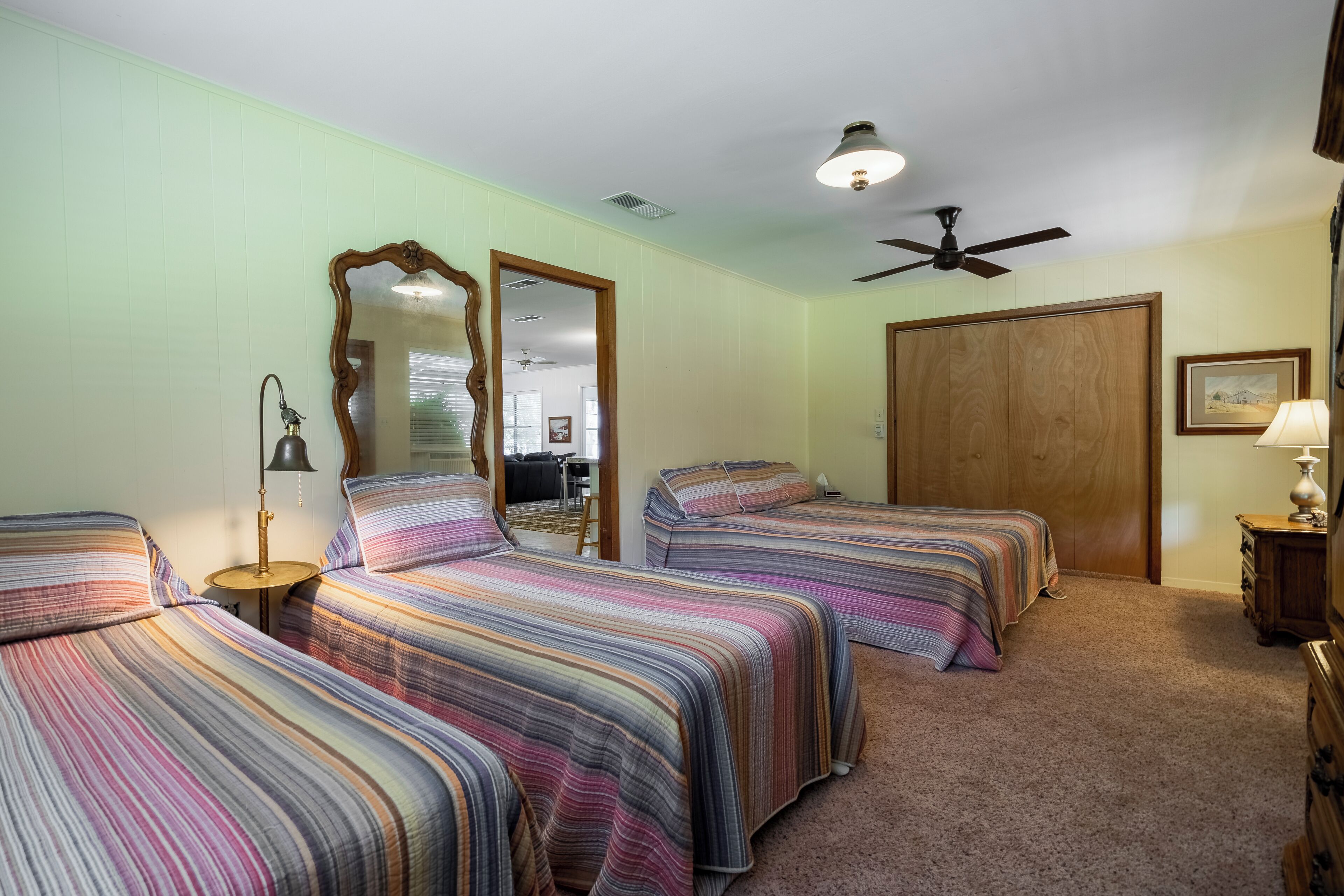 A room with three beds, a ceiling fan, and a large mirror.