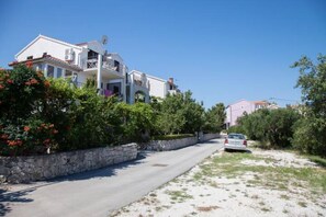 A residential street with houses, a stone wall, and a parked car. - Apartment Sonja Supetar - Ap.no. 1 (Supetar)