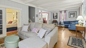 En stue med en grå sofa, en blå sofa, et træbord og en rund skammel. Der er en trappe, der fører til et andet rum.