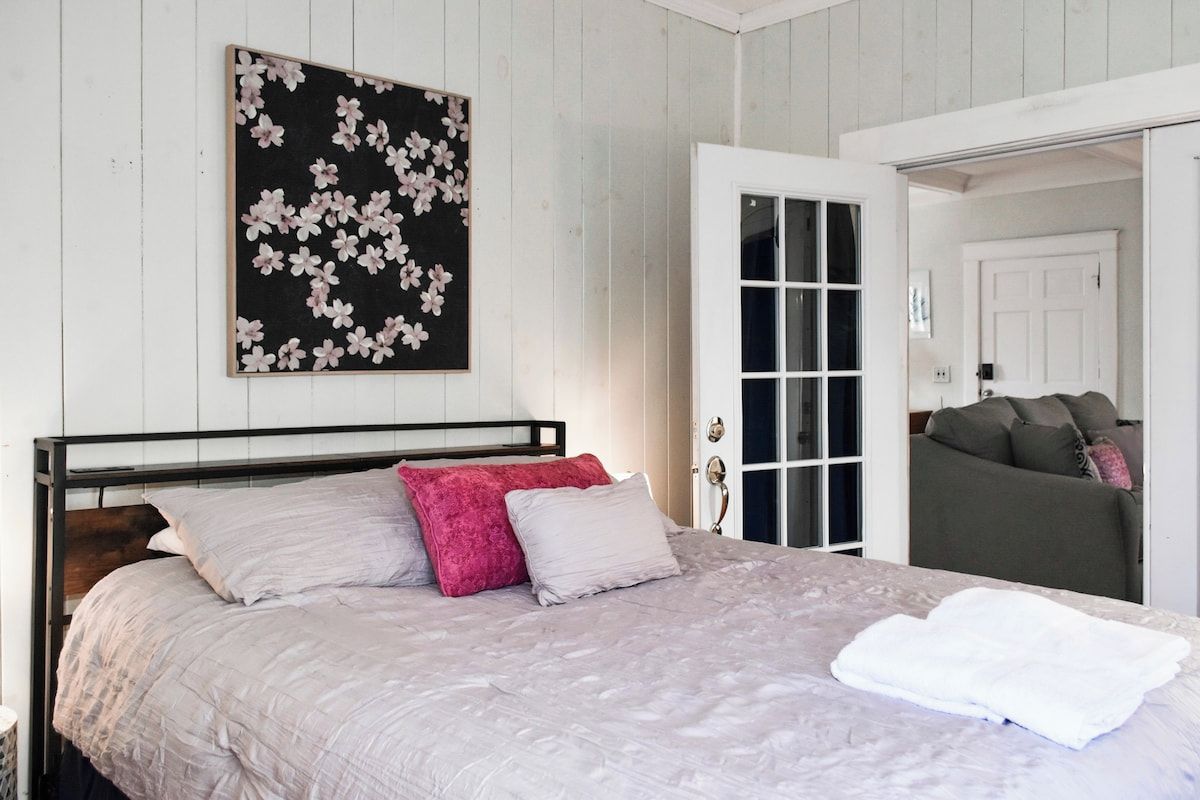 A bedroom with a bed, pillows, a door, and a wall-mounted picture.