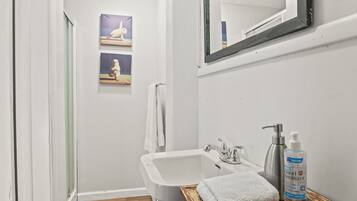 Un baño con lavamanos blanco, tocador de madera, botella de gel antibacterial y espejo.