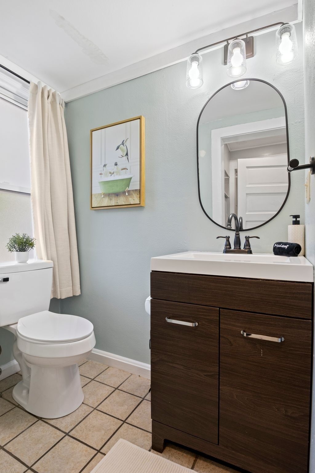 A bathroom with a toilet, vanity with a mirror, and a framed picture on the wall.